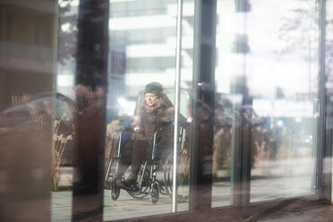 Reflection of woman in wheelchair on glass windows of building - CUF48954