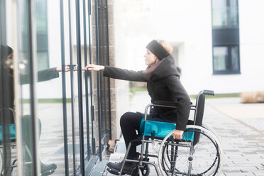 Woman in wheelchair opening door to building - CUF48958