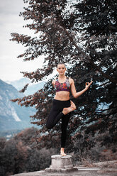 Woman practicing yoga, balancing on one leg on top of plinth, mountain landscape, Domodossola, Piemonte, Italy - CUF49003