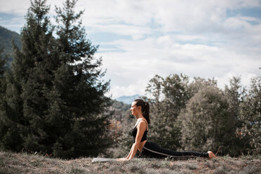 Frau übt Yoga, auf Yogamatte in ländlicher Landschaft - CUF49007