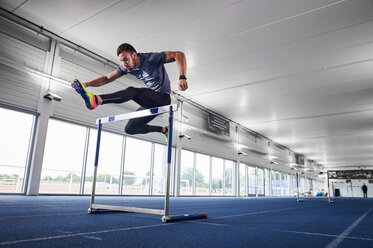 Athlete jumping over hurdle on indoor running track - CUF49067