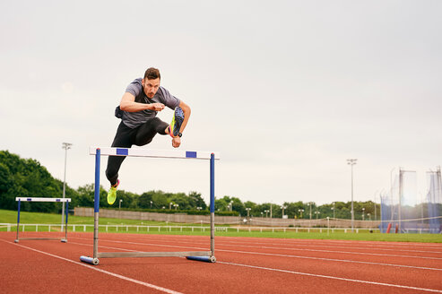 Athlete jumping over hurdle on running track - CUF49068