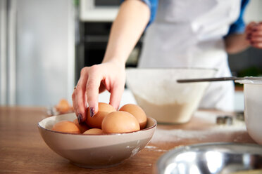 Woman taking egg from bowl in kitchen - CUF49113