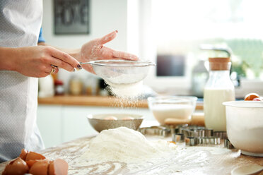 Woman sifting flour in kitchen - CUF49122