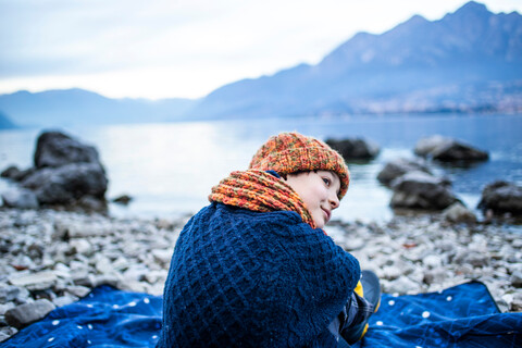 Junge sitzt auf einer Decke am Seeufer, Comer See, Onno, Lombardei, Italien, lizenzfreies Stockfoto