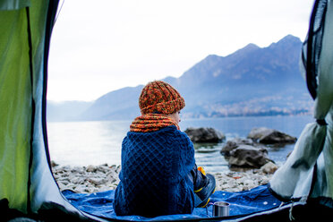 Boy sitting on blanket by tent, rear view, Lake Como, Onno, Lombardy, Italy - CUF49157