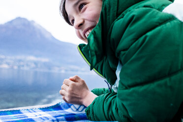 Junge im grünen Anorak auf Picknickdecke am Seeufer liegend, Ausschnitt, Comer See, Onno, Lombardei, Italien - CUF49224