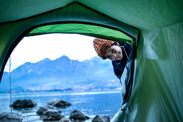 Boy peering into tent by lakeside, Onno, Lombardy, Italy - CUF49237