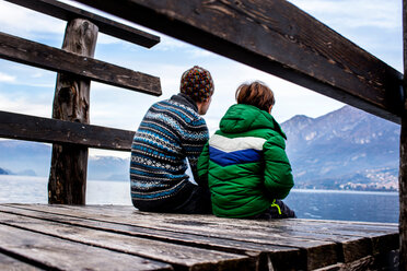 Junge und Vater sitzen auf einem Steg am See, Rückansicht, Comer See, Onno, Lombardei, Italien - CUF49251