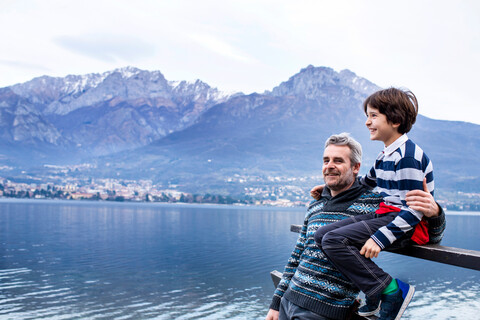 Boy and father sitting on pier fence, Lake Como. Onno, Lombardy, Italy stock photo