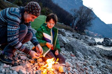 Father and son toasting marshmallows over campfire, Onno, Lombardy, Italy - CUF49260