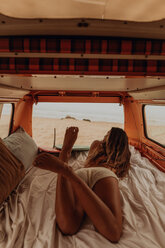 Young female surfer looking out from back of recreational vehicle at beach, Jalama, California, USA - ISF20522