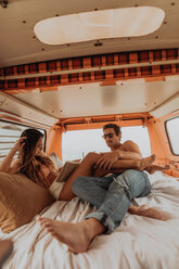 Young surfing couple reclining in back of recreational vehicle at beach, Jalama, California, USA - ISF20526