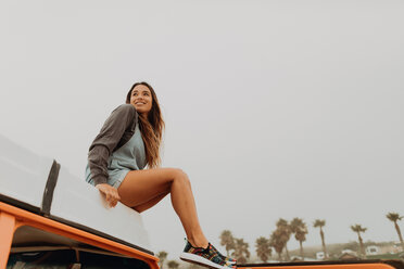 Young woman sitting on recreational vehicle roof at beach, Jalama, California, USA - ISF20540