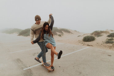 Junges Paar hält sich an den Händen und teilt sich ein Skateboard auf einem Strandparkplatz, Jalama, Kalifornien, USA - ISF20551