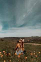 Junge Frau sitzt in einem Feld mit Wildblumen und schaut nach oben, Jalama, Kalifornien, USA - ISF20565