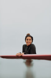 Young female surfer leaning on surfboard in calm misty sea, portrait, Ventura, California, USA - ISF20595