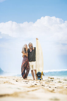 Älteres Hippie-Paar mit Surfbrett am Strand stehend - SBOF01707