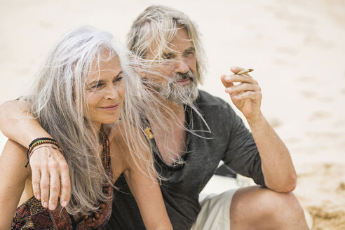 Porträt eines älteren Hippie-Paares beim Rauchen am Strand - SBOF01708