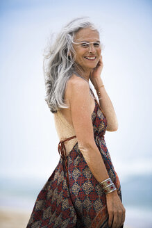 Portrait of smiling senior hippie woman with sandy back on the beach - SBOF01718