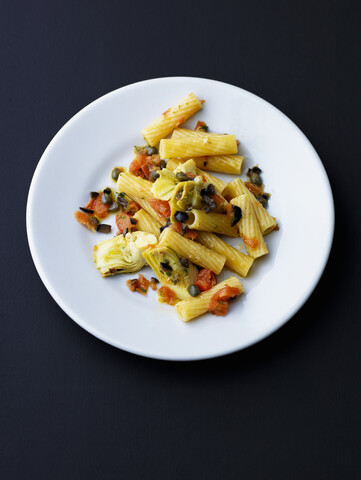 Teller mit Tortiglioni mit Artischocken, Oliven, Tomaten und Kapern, lizenzfreies Stockfoto