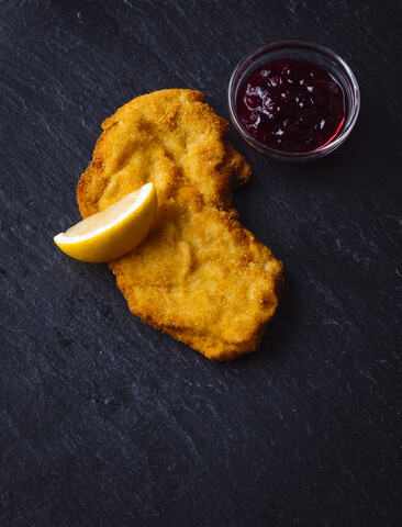 Wiener Schnitzel, Zitronenscheibe und Schale mit Preiselbeersauce auf Schiefer, lizenzfreies Stockfoto