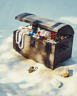 Treasure chest filled with jewels and gold coins on sandy beach - PPXF00173