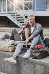 Lachender reifer Mann und junge Frau mit Sporttasche vor einer Turnhalle sitzend - RORF01715