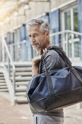 Porträt eines reifen Mannes mit Sporttasche, der vor einem Fitnessstudio steht - RORF01719