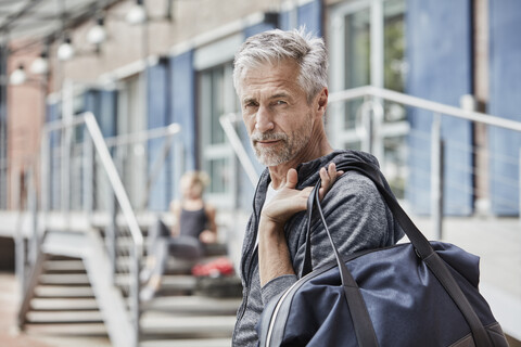 Porträt eines reifen Mannes mit Sporttasche vor einem Fitnessstudio, lizenzfreies Stockfoto