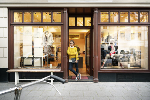 Young woman standing in door of a fashion store, holding laptop - PESF01390