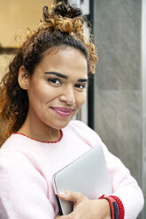 Junge Frau steht in der Tür eines Modegeschäfts und hält einen Laptop - PESF01406