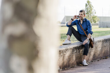 Man on the phone sitting on a wall outdoors - GIOF05704