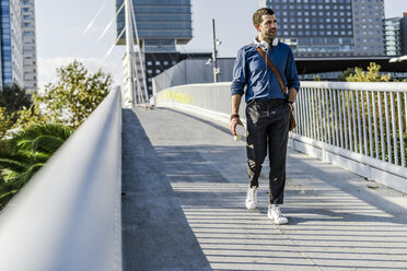 Man with headphones and coffee to go walking on a footbridge - GIOF05725