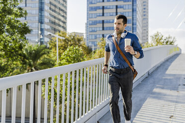 Porträt eines Mannes mit Kaffee zum Laufen auf einer Brücke - GIOF05726