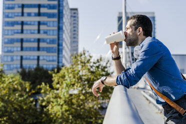 Profile of man leaning on railing drinking coffee to go - GIOF05727