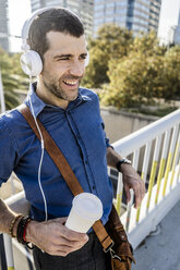 Porträt eines lächelnden Mannes mit Kaffee zum Mitnehmen, der mit Kopfhörern Musik hört - GIOF05730