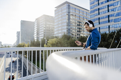 Mann hört Musik mit Kopfhörern und Smartphones auf einer Brücke - GIOF05735