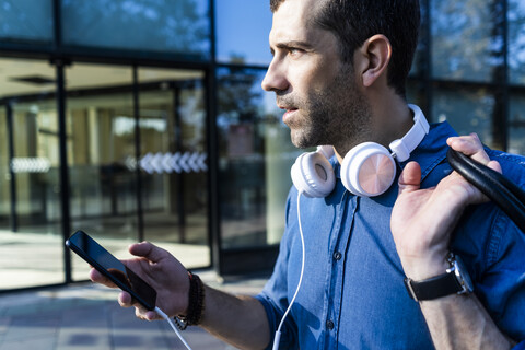 Profil eines Mannes mit Kopfhörern und Mobiltelefon, der in die Ferne schaut, lizenzfreies Stockfoto