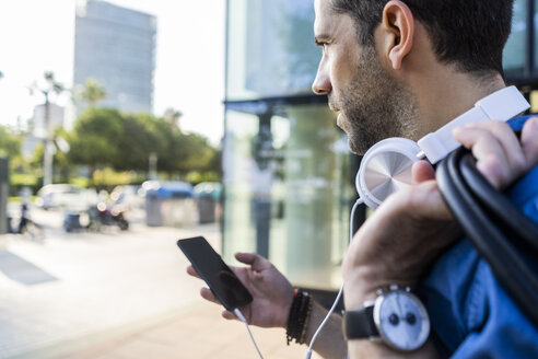 Mann mit Kopfhörern und Mobiltelefon schaut in die Ferne - GIOF05742