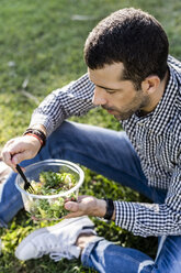 Mann sitzt auf einer Wiese im Stadtpark und isst gemischten Salat - GIOF05743