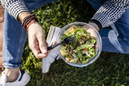 Man sitting on a meadow eating mixed salad, partial view - GIOF05744