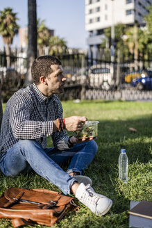 Mann sitzt auf einer Wiese im Stadtpark und isst gemischten Salat - GIOF05745