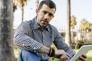 Portrait of man sitting in city park with digital tablet - GIOF05761
