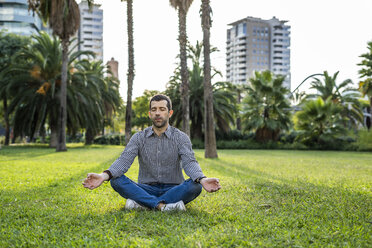 Mann sitzt auf einer Wiese im Stadtpark und macht Yogaübungen - GIOF05763
