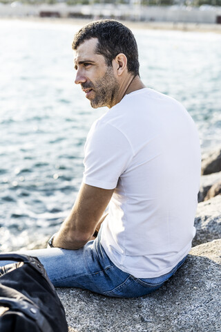 Mann sitzt auf einem Felsen vor dem Meer und entspannt sich, lizenzfreies Stockfoto