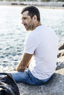 Mann sitzt auf einem Felsen vor dem Meer und entspannt sich - GIOF05766