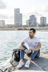 Spain, Barcelona, man sitting on a rock in front of the sea looking at distance - GIOF05767