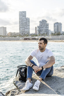 Spanien, Barcelona, Mann sitzt auf einem Felsen vor dem Meer und schaut in die Ferne - GIOF05767