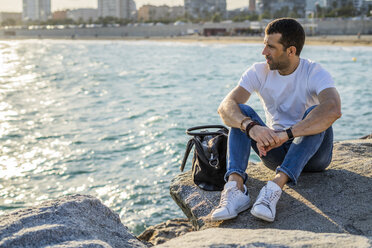 Spain, Barcelona, man sitting on a rock in front of the sea looking at distance - GIOF05768